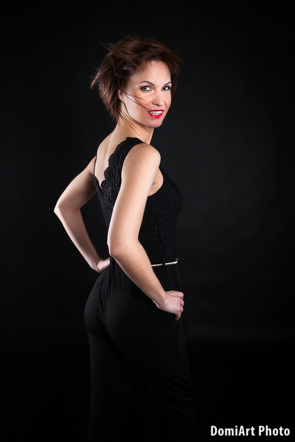 Visszaforduló női modell, rövid fazonú hajjal, szélgéppel, fekete háttér előtt fekete ruhában. Műtermi fotózás