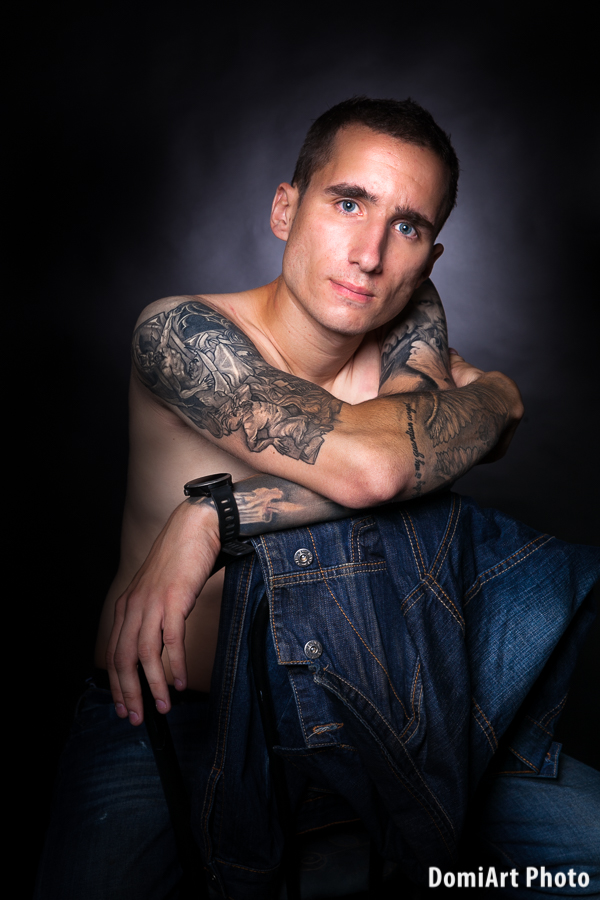 prémium férfi profil fotózás - tetovált kezű férfi úl a széken fekete háttér előtt