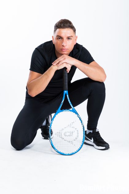 teniszütőre támazkodó gugoló srác, sportos öltözetben - férfi portré