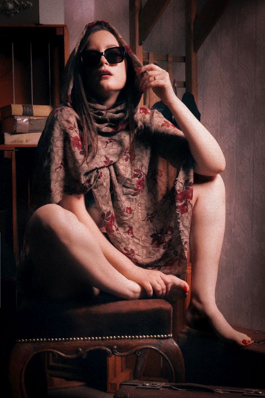 virágokkal a kezében ül félmeztelenül a lány a széken, de a felsőtestét a virágok eltakarják