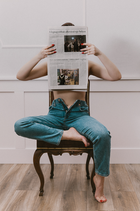 lifestyle glamour fotózás egy barna széken ül egyenesen egy lány, hatalmas újságot tartva maga előtt