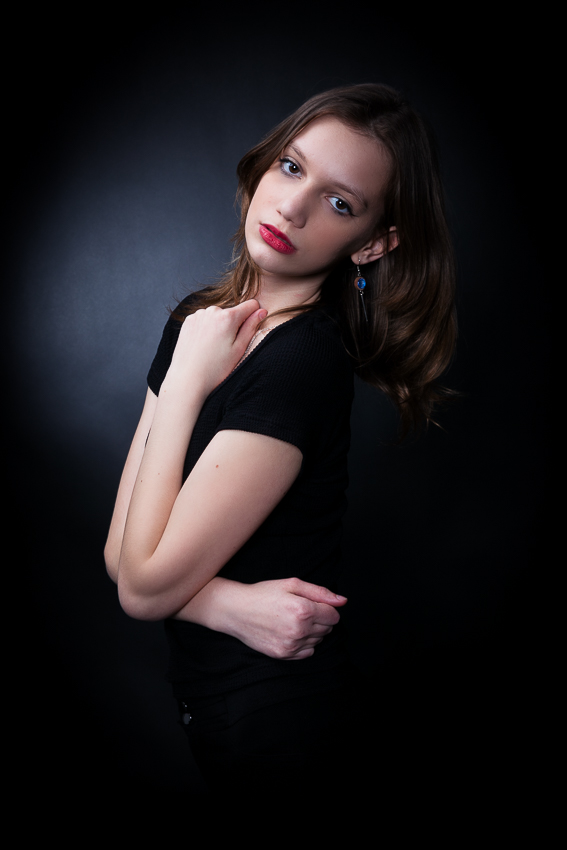 modell headshot portré karakteres világítással,modell portfólió készítés fekete harisnya és fekete body a modellen, görnyedt pózban a fekete széken ül, fekete háttér előtt - debrecen